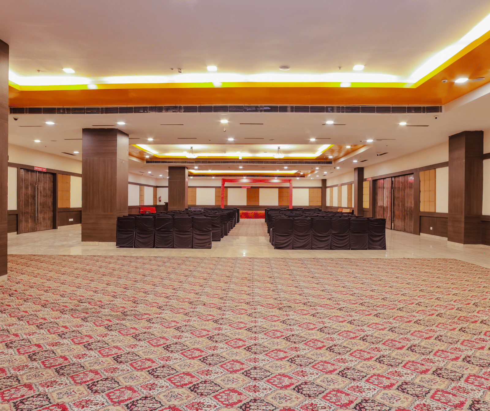 A large, empty ballroom or banquet hall with a patterned carpet, high ceilings, and a stage or raised platform at the far end, ready for an event.