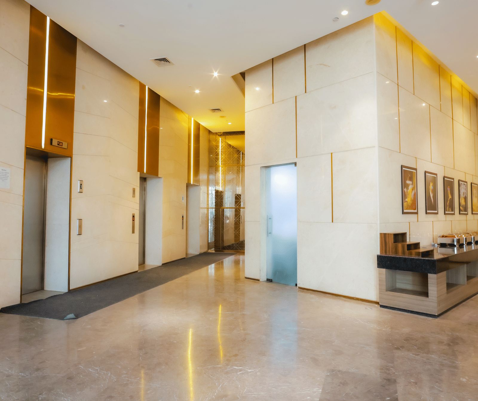 A clean and well-lit hotel corridor or waiting area with modern wall panelling, subtle lighting, and a long bench for seating.