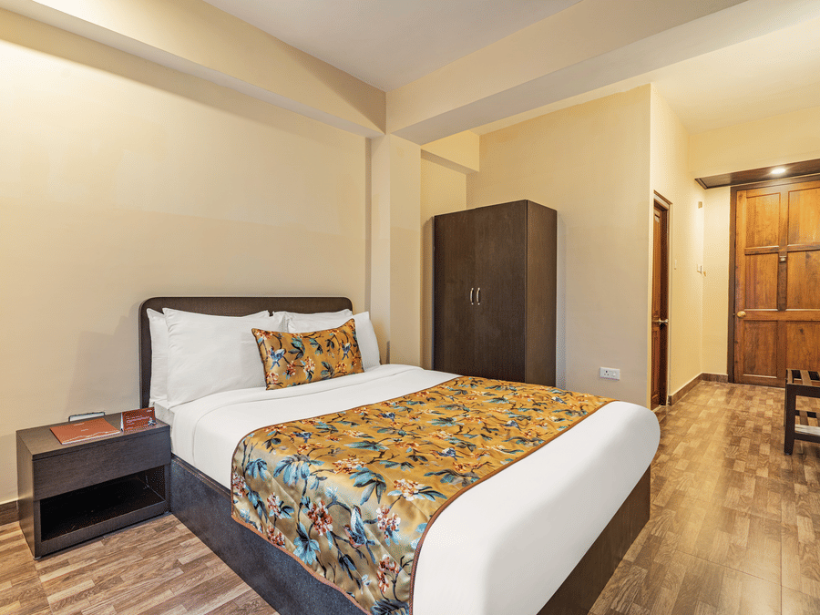 Comfortable hotel room with a double bed, floral yellow bedding, bedside table, wardrobe, and wooden flooring near the entrance door - Summit Namnang Courtyard & Spa, Gangtok
