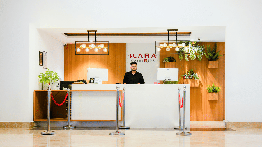 Front desk with a white counter, queue stanchions, wall planters and twin pendant lights beneath the hotel logo at Ilara Hotels & Spa, Tada.