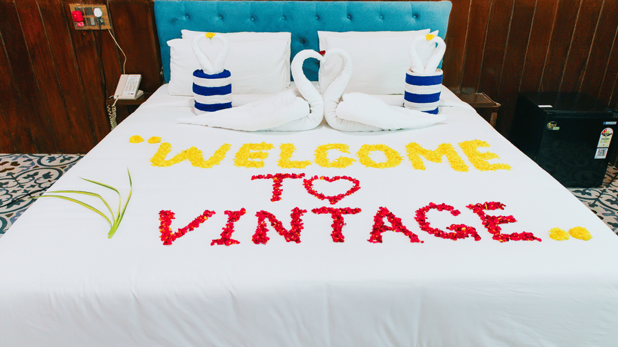 A double bed with a blue headboard decorated with flower petals spelling WELCOME TO VINTAGE and towel art swans | Vintage Trails By Ilara