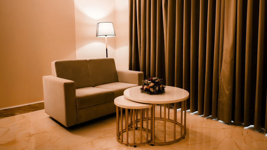 Seating corner of the Junior Suite with a beige sofa, floor lamp and round nesting tables holding fresh flowers at Ilara Hotels & Spa, Tada.