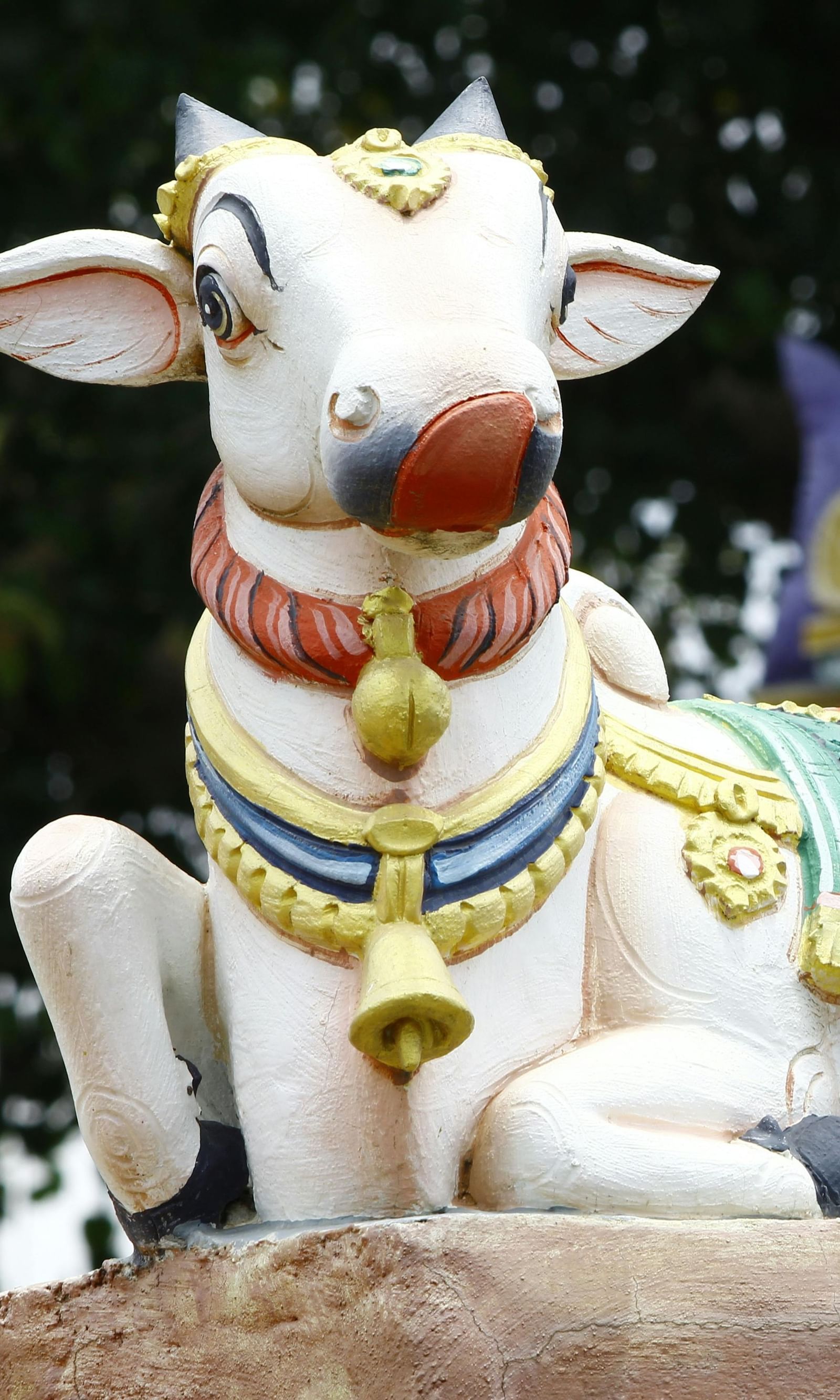 A beautifully painted Nandi statue sits outdoors, surrounded by temple carvings - Grand Madurai by GRT hotels.
