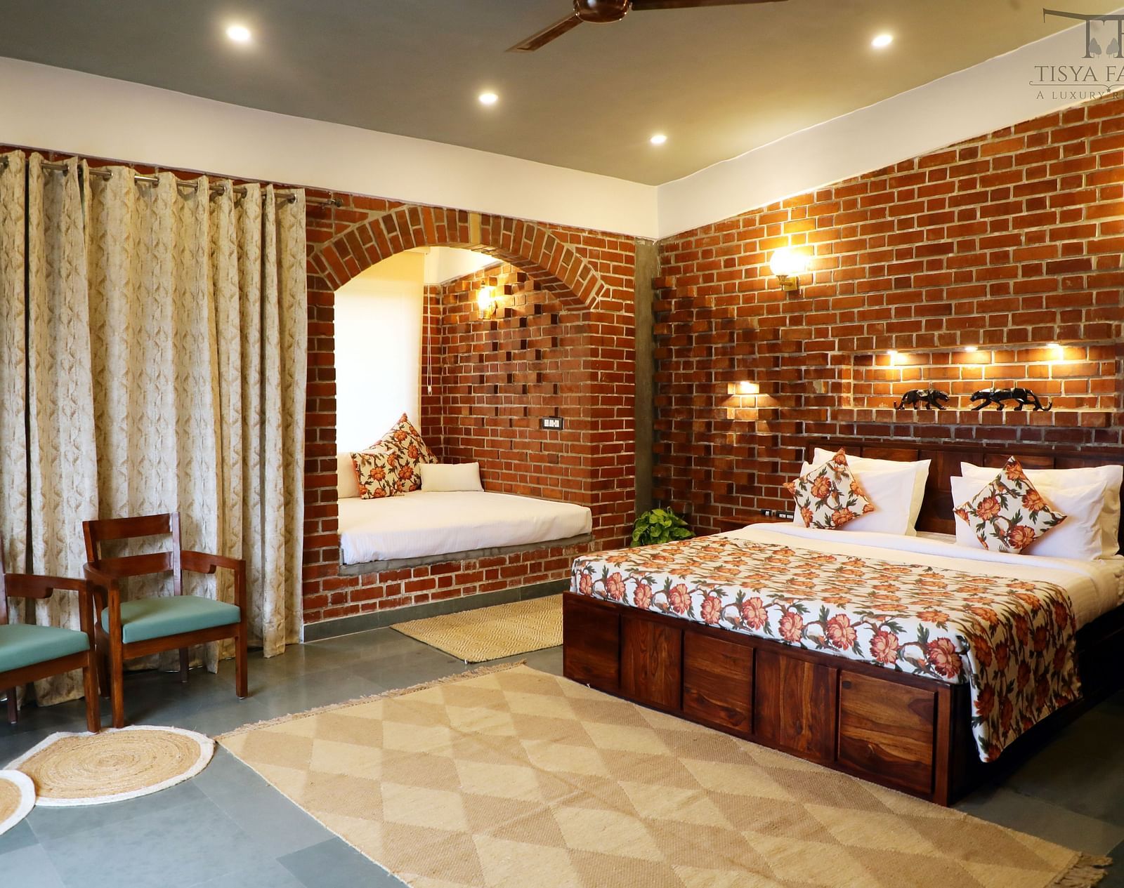A bedroom at Tisya Farms, Gurgaon with a double bed, chairs, brick walls, curtains, and overhead lighting.