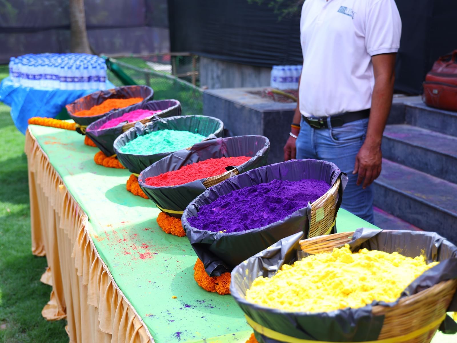 A person stands next to a table with multiple large bowls filled with colourful powders | Vedic Village Spa Resort, Kolkata