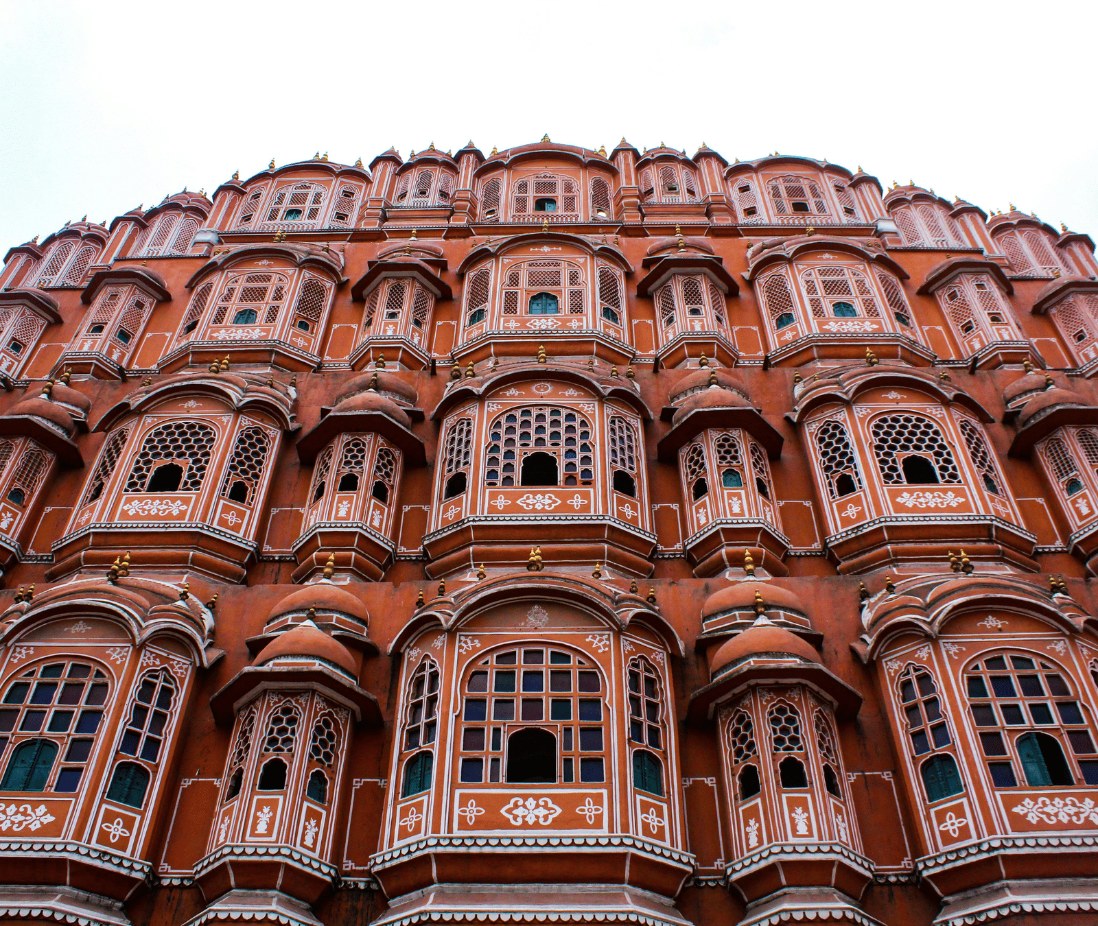 A low-angle view of the Hawa Mahal's 5-storey pink sandstone facade with its many ornate jharokha windows.