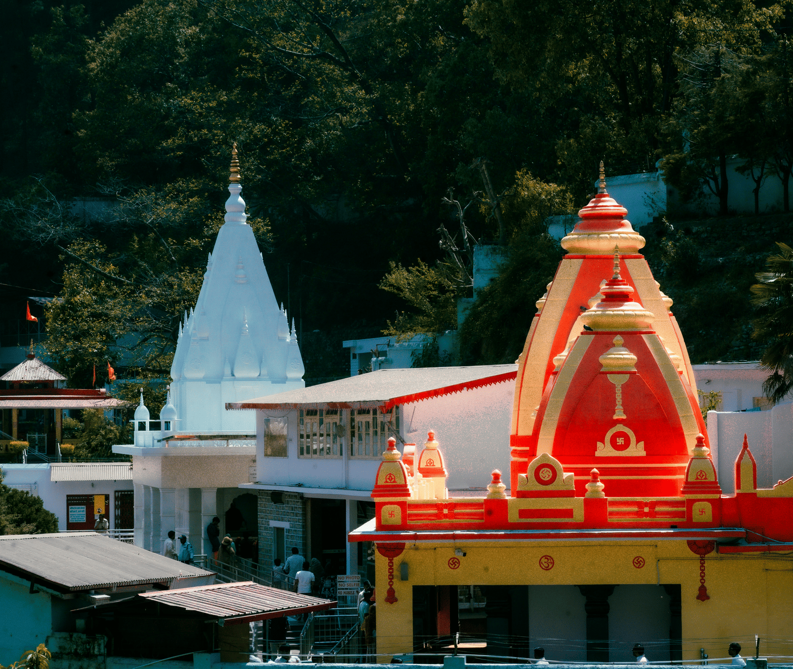 A brightly coloured yellow and red temple sits at the bottom of a green mountain.