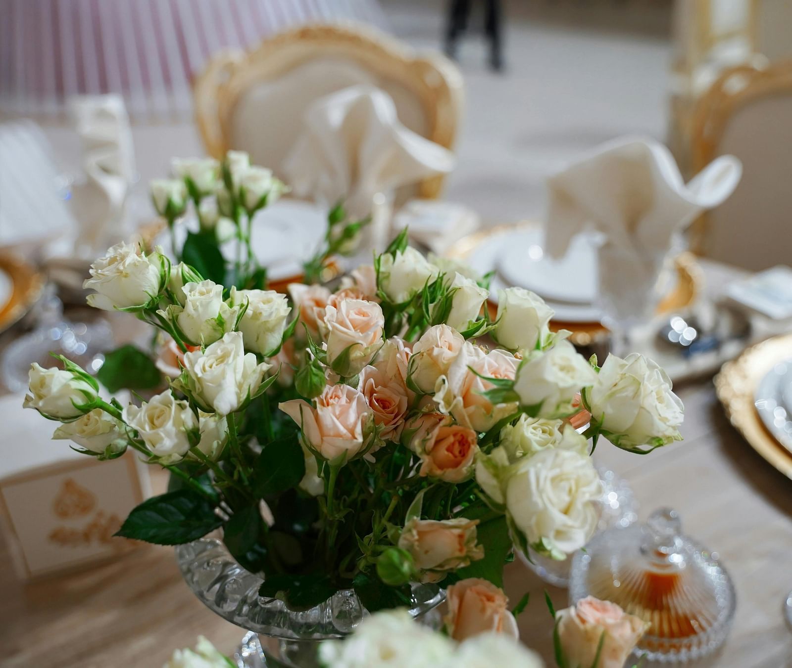 A close up shot of a beautiful flower vase with a lot of white and pink roses on a dining table.