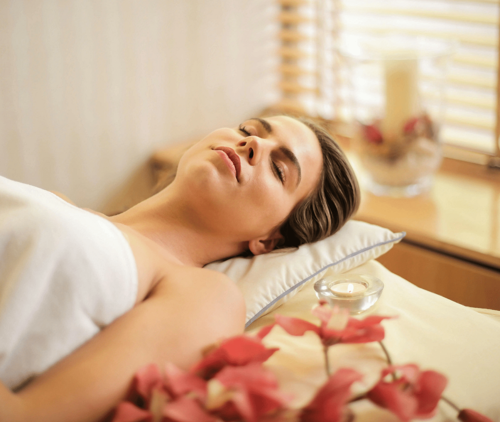 A woman with her eyes closed lying down on a spa bed alongside a small candle.