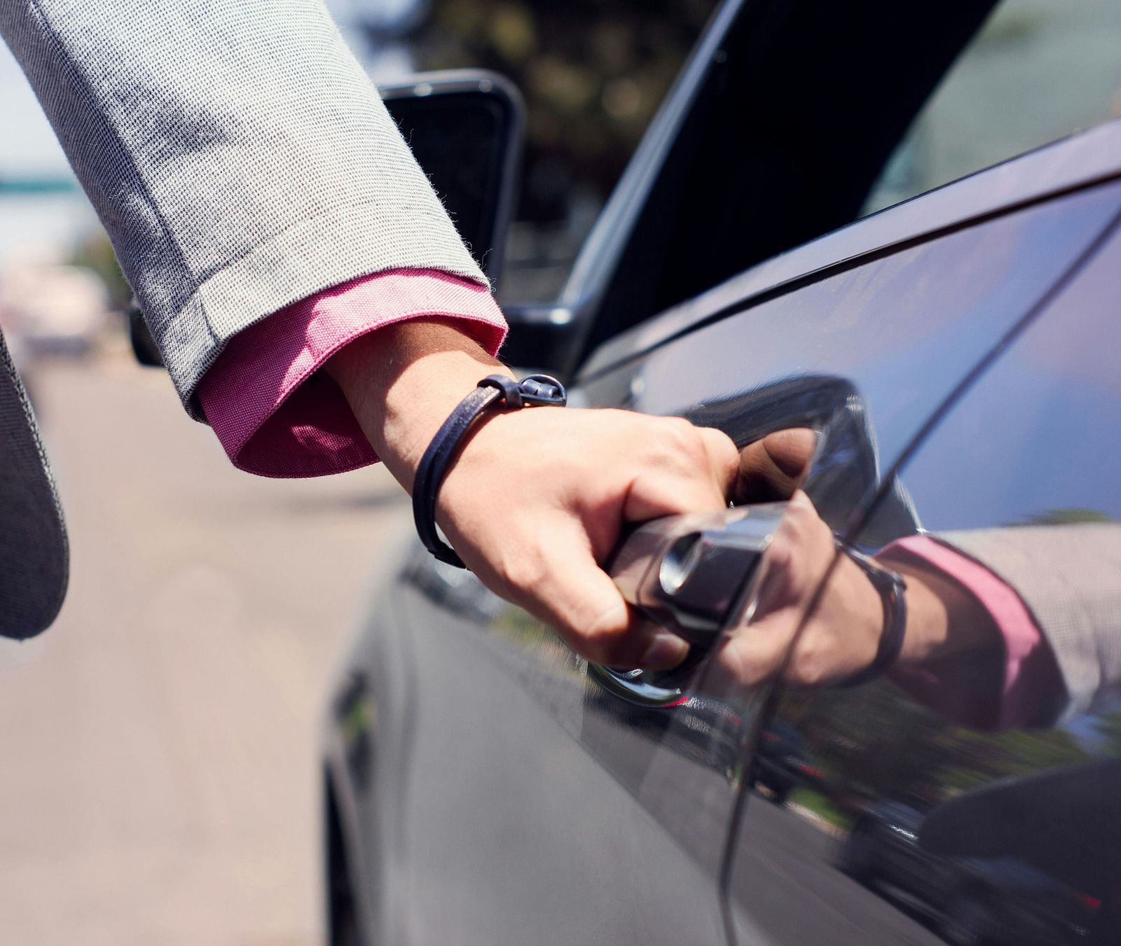 A person dressed in business formals opening the door of a car.