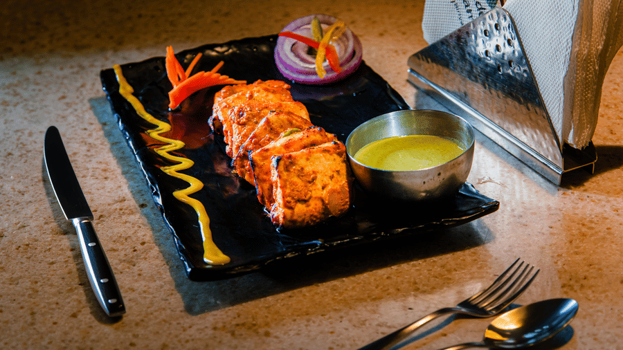 Row of tandoori tikka slices with a sauce drizzle, green chutney, onion rings and a carved carrot fan at Tandoori Tamashaa, Ilara Hotels & Spa, Tada.