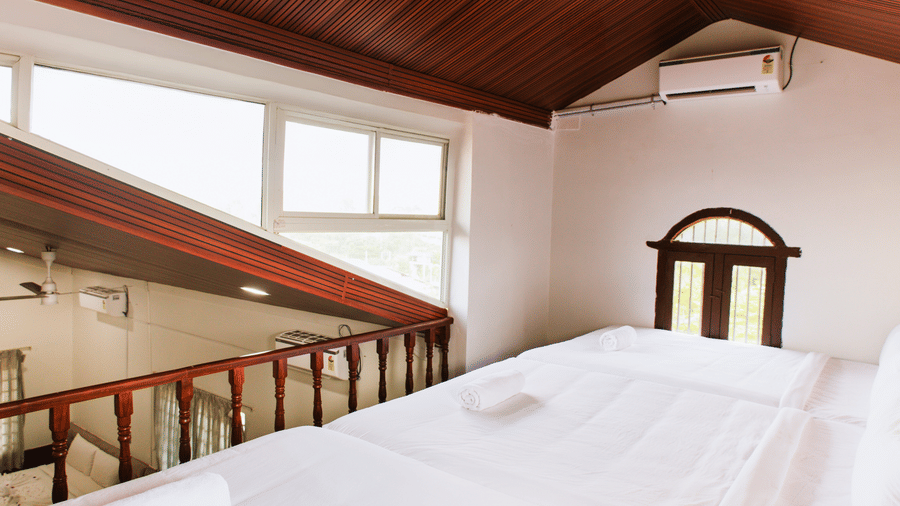 A loft bedroom area under a sloped wooden ceiling with white bedding and a protective wooden railing | Vintage Trails By Ilara
