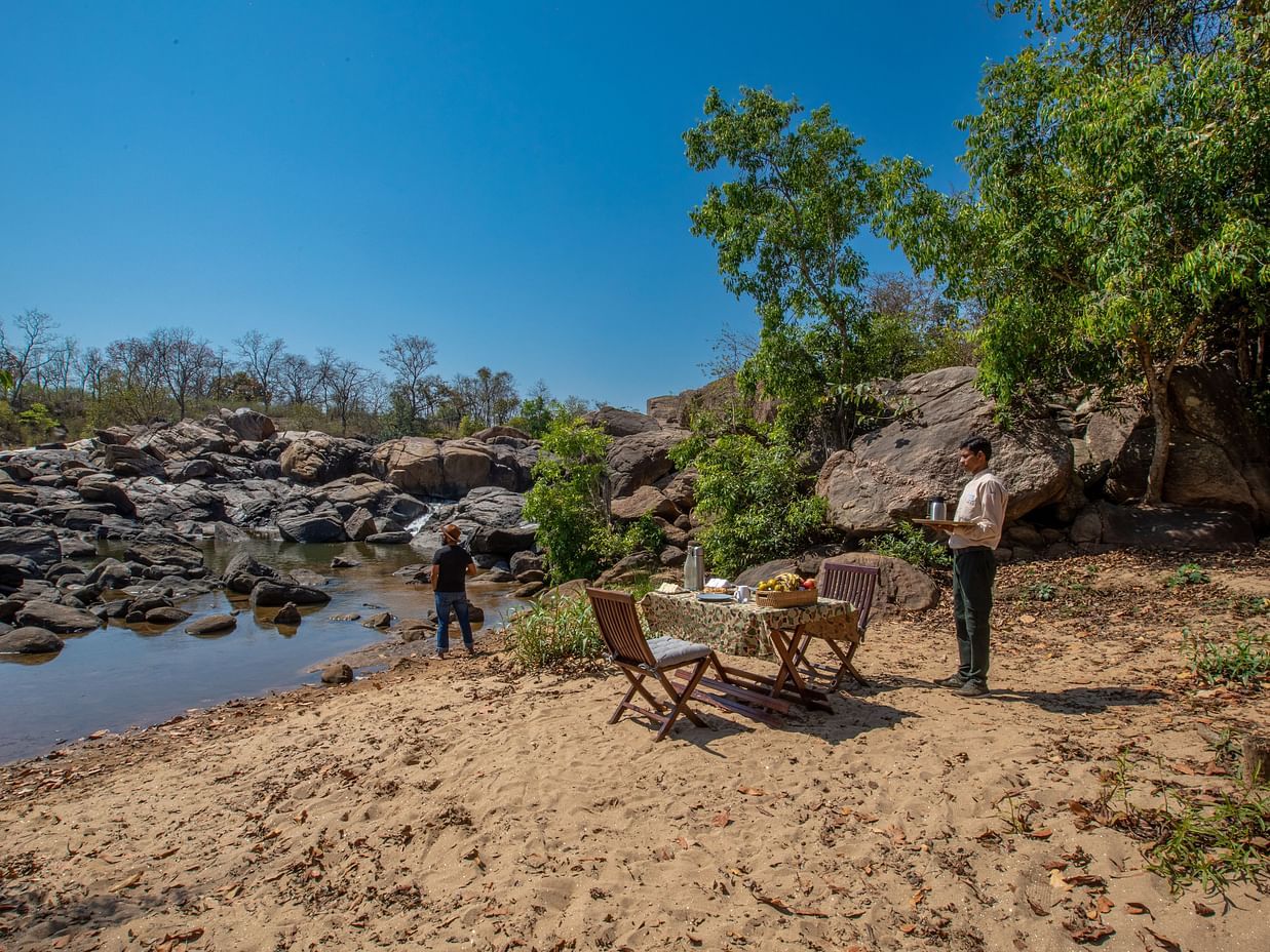 Dining arrangement besides a waterbody at The Riverwood Forest Retreat, Kanha 