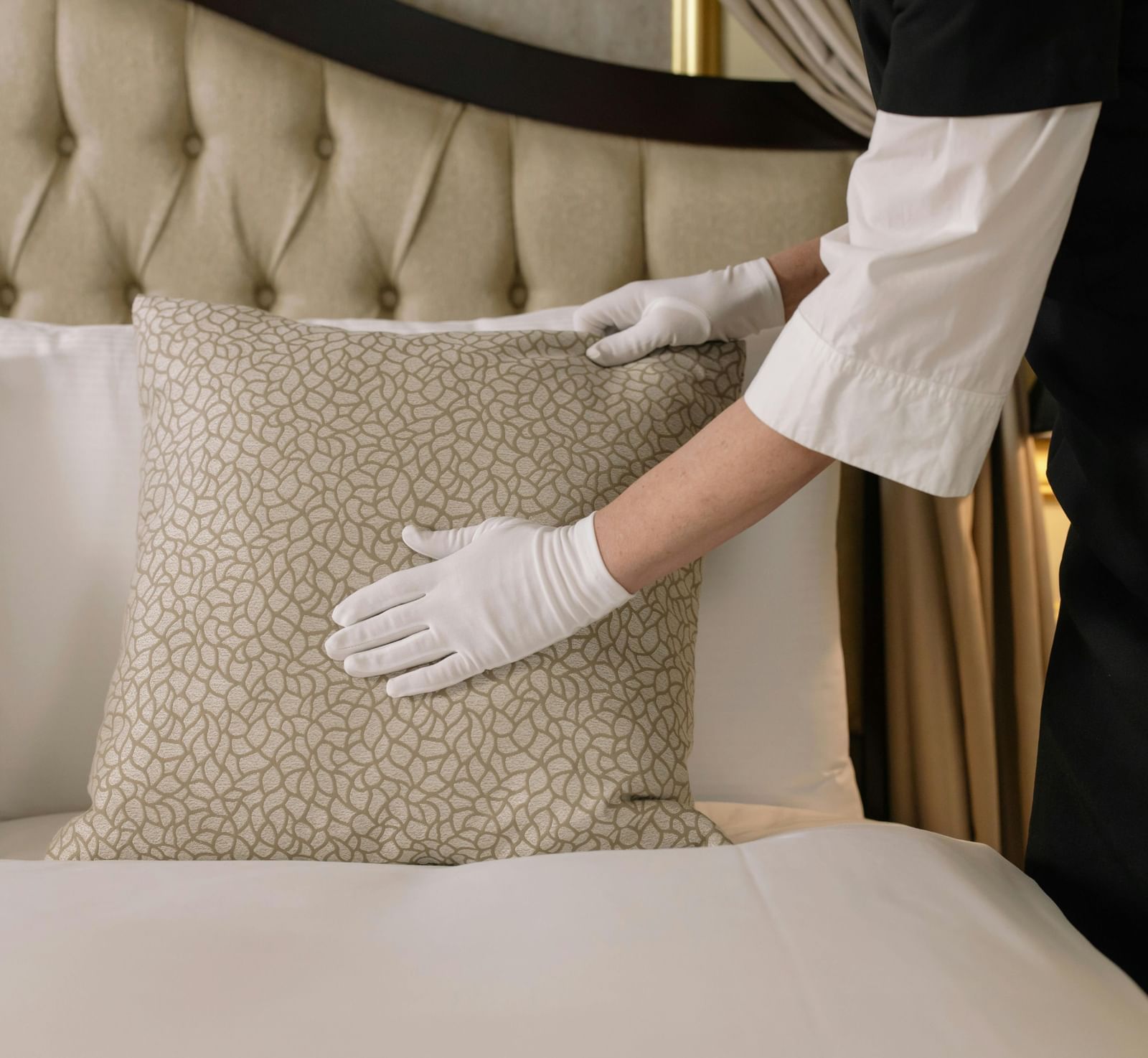 A housekeeper wearing white hand gloves making the bed at a hotel room.