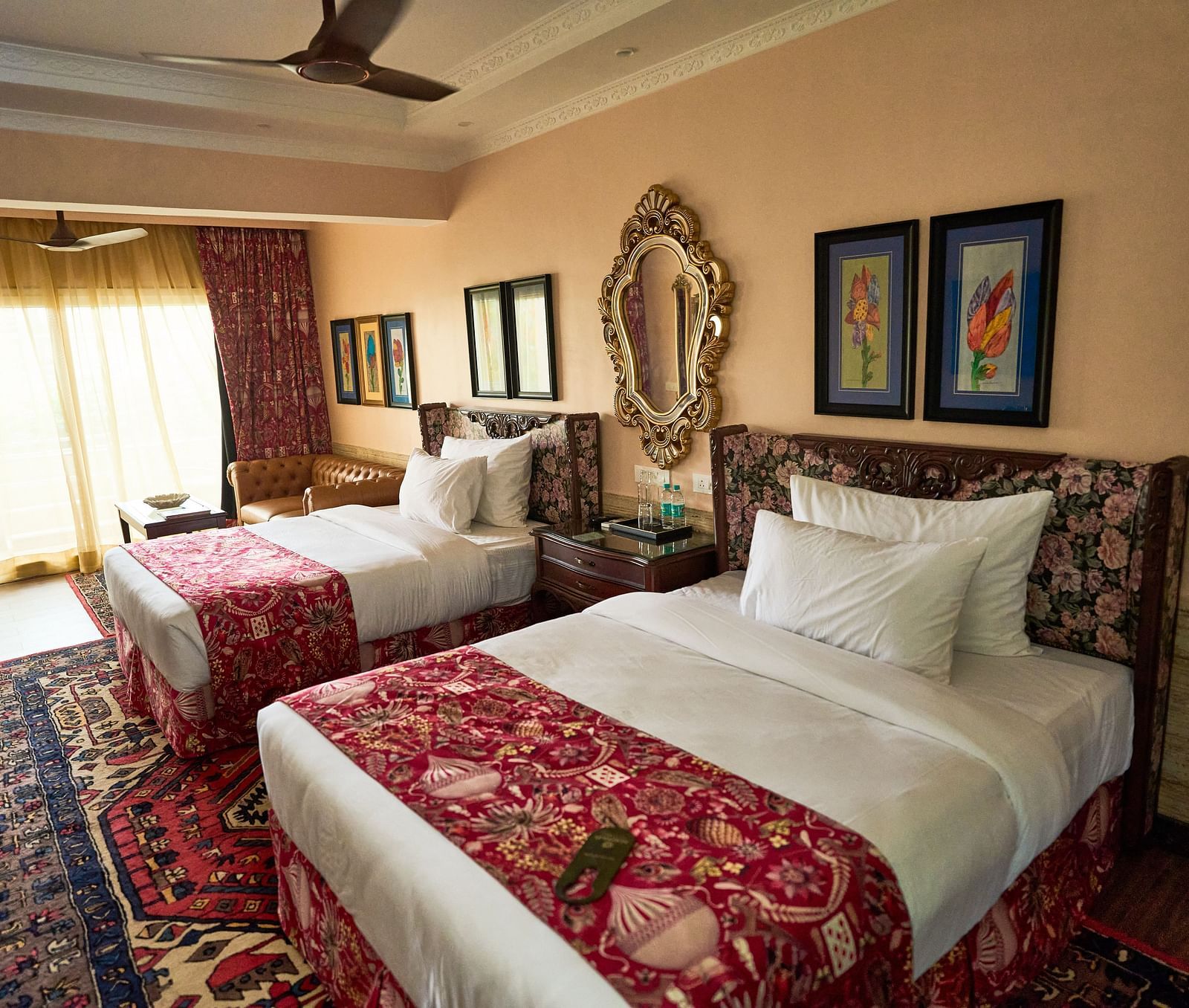 Side view of a spacious room featuring a double bed, wall-mounted frames for decoration, and windows elegantly covered with curtains at Mayfair Manor, Alibag