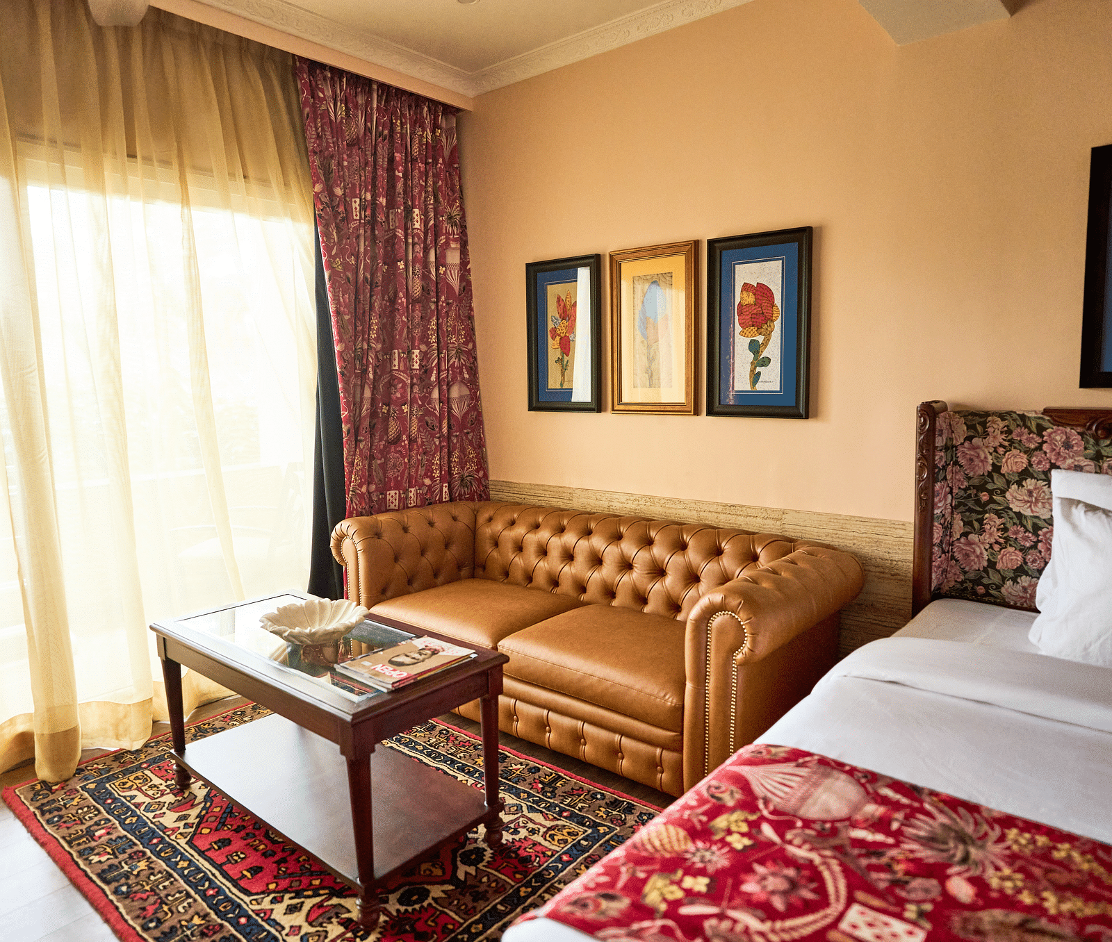 A spacious room featuring a bed on one side, a cushioned sofa on the other, and a glass table near the window adorned with closed curtains at Mayfair Manor, Alibag