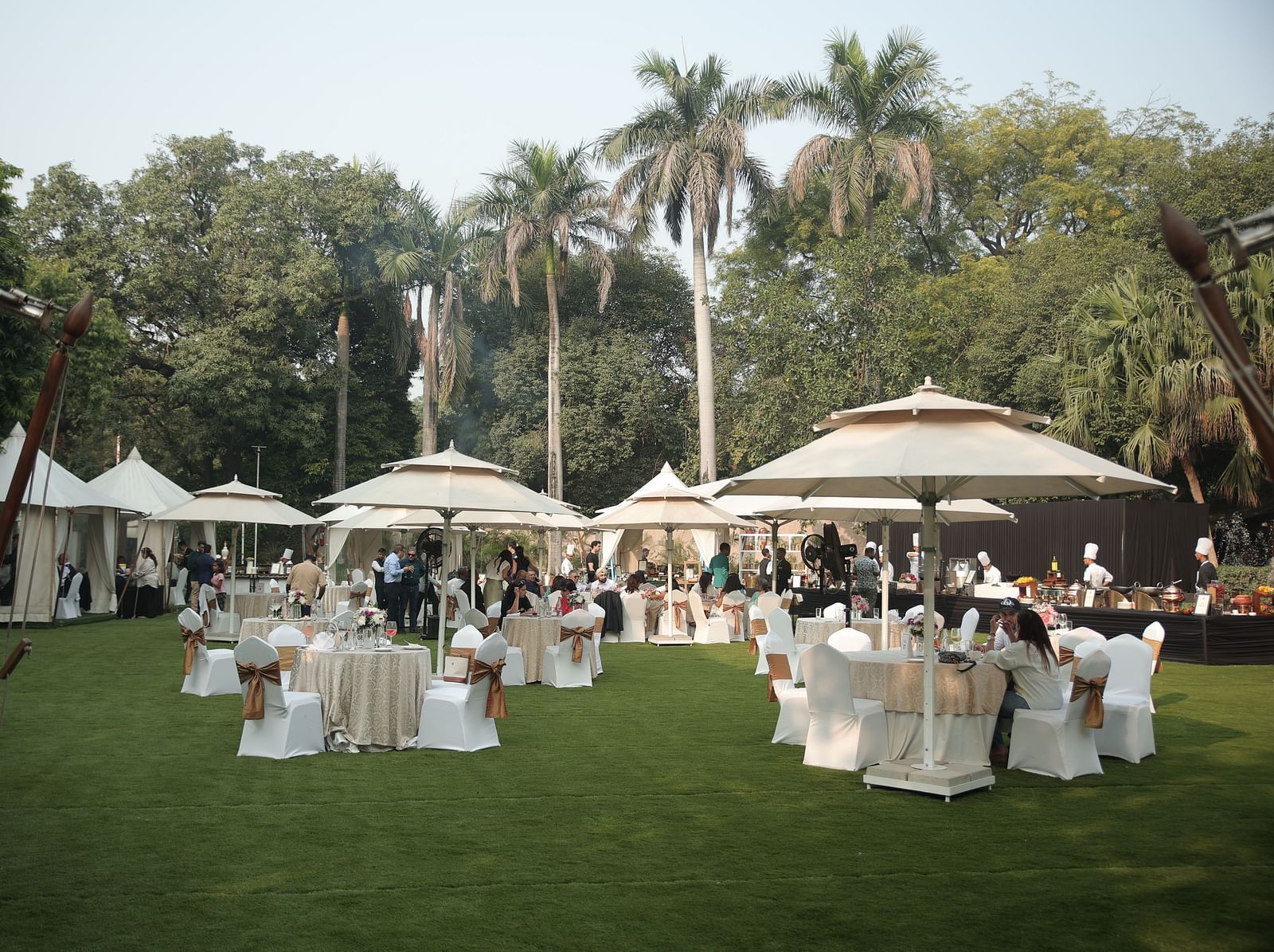 Image of the spacious garden at The Claridges New Delhi, featuring an open area with a clear sky, surrounded by large trees