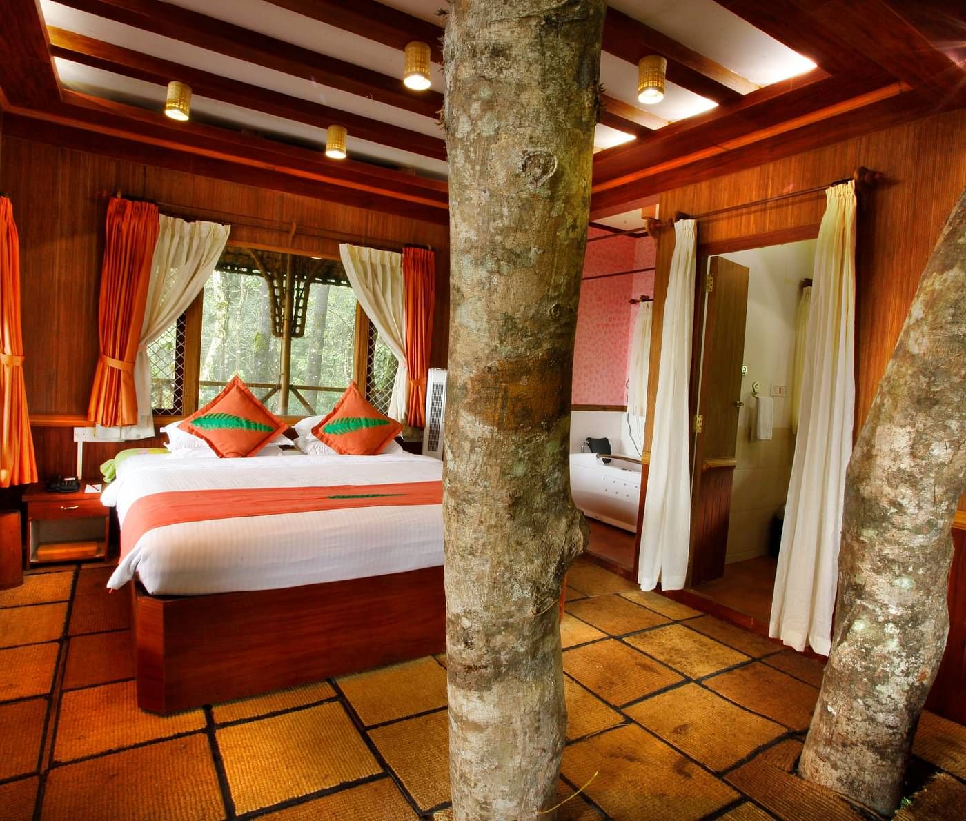 Room with a bed and tree trunks protruding out of the floor at Vythiri Resort, Wayanad