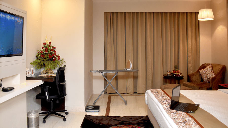 A well-appointed hotel room at Lords Plaza Surat featuring a bed, desk, television and an ironing table 