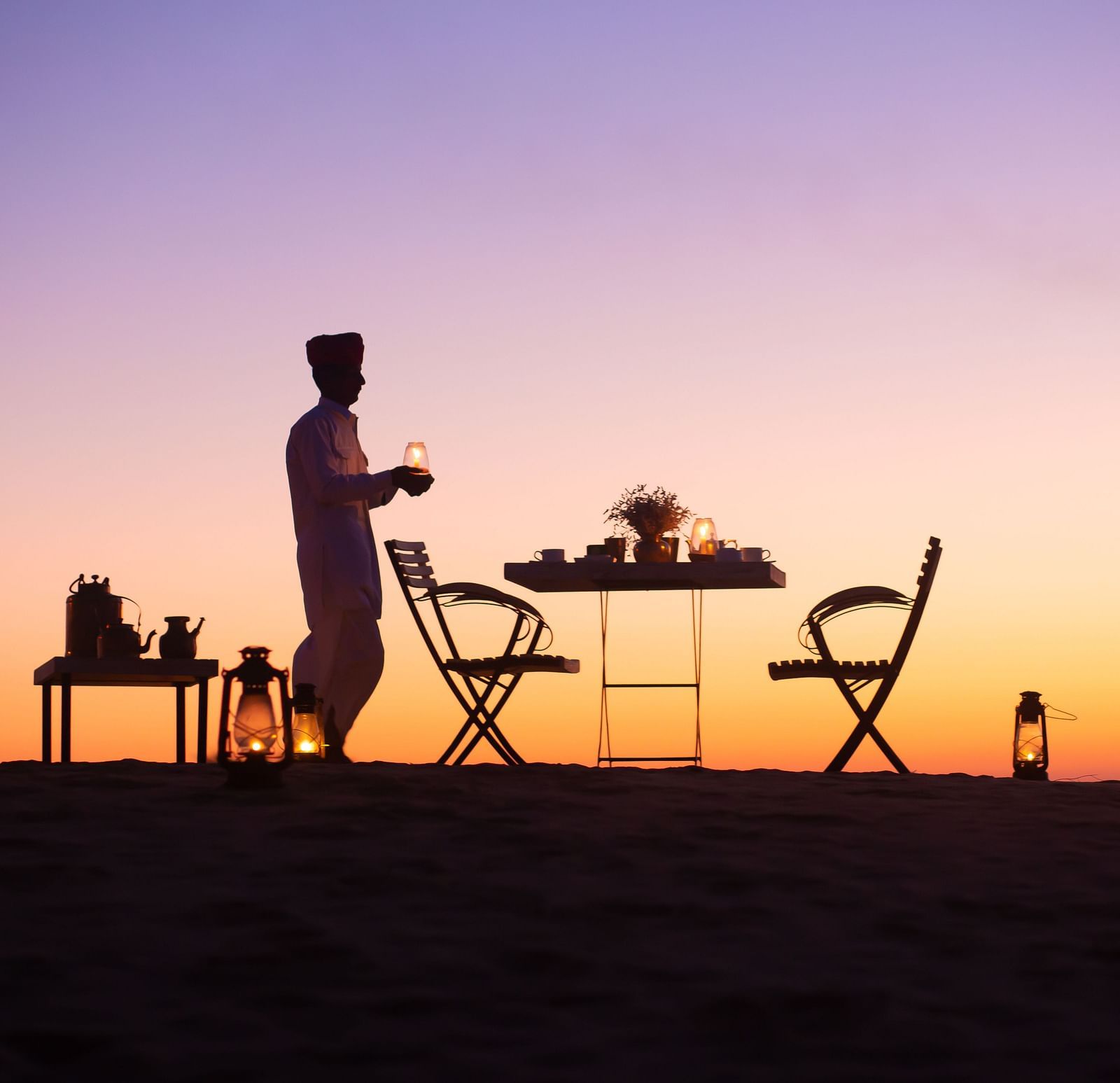 A man with a table a table and a chair in a sunset view - MANVAR Resort & Desert Camp