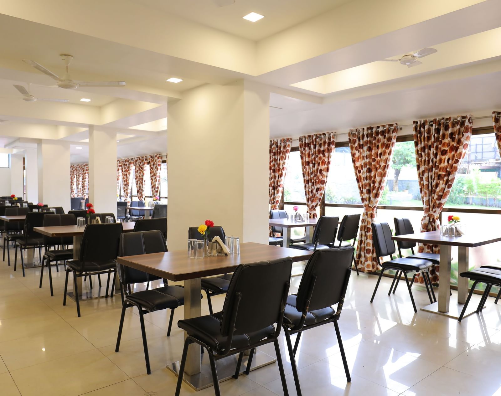 Dining tables in the spacious Darbar Restaurant that has glass windows through which natural light seeps in, at Highland Resort.