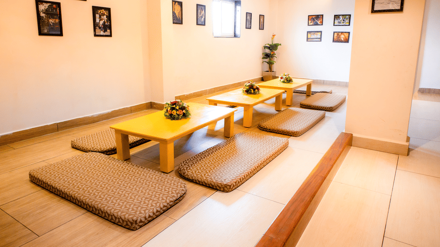 Low wooden tables with floral centrepieces and patterned floor cushions beneath framed Japanese art at Ajito, Ilara Hotels & Spa, Tada.