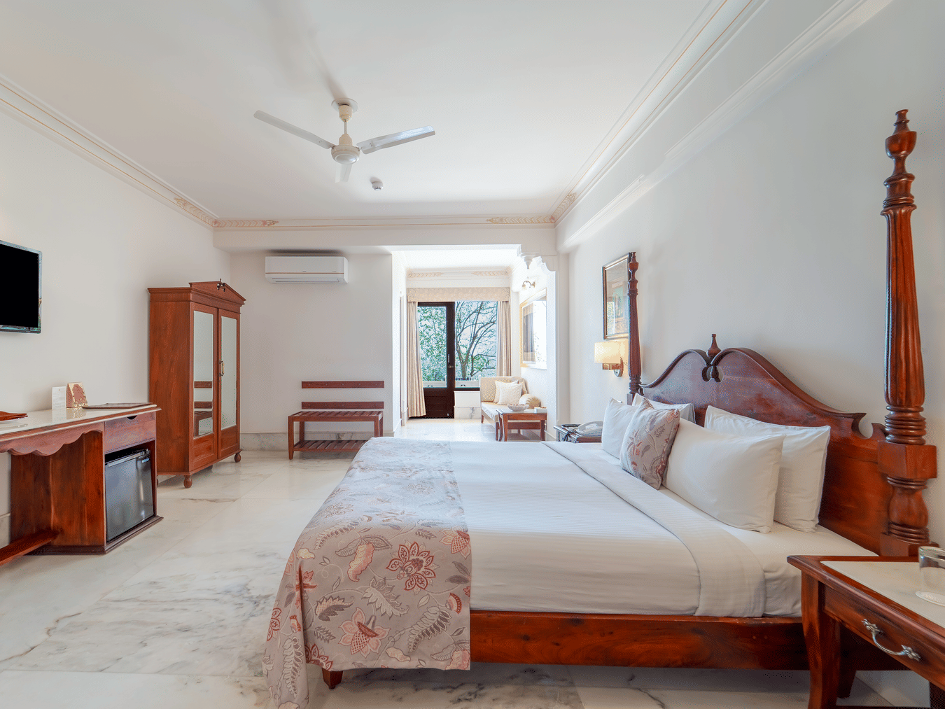 A wide view of a grand suite featuring a king size bed, dark wood furniture, and a wall-mounted television - Fateh Garh, Udaipur