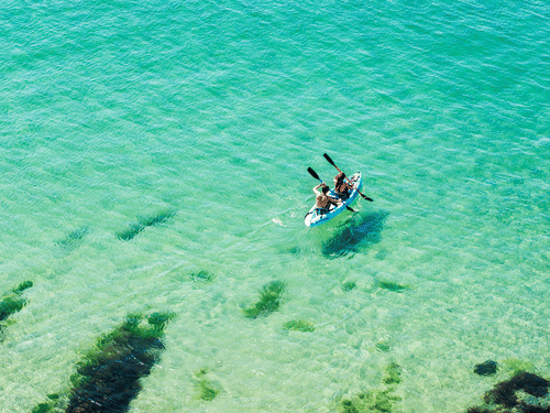 Aerial view of two people kayaking in clear turquoise water near the shore