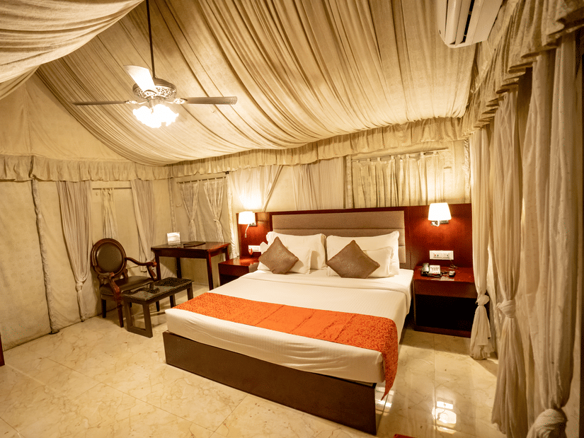 Cottage Room at Pride Hotel and Convention Centre, Indore featuring a plush bed with two nightstands on both sides and lamps mounted on them and a sitting space next to it