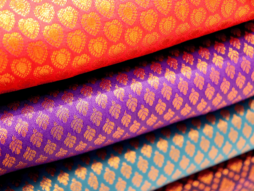Multiple folded saree pieces with patterned textile designs in different colours stacked on top of each other.