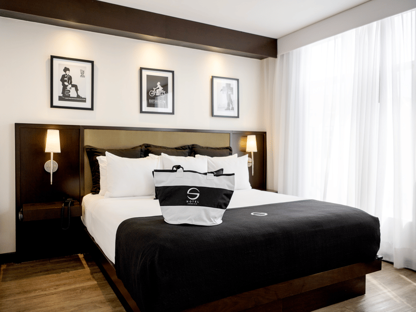 The Standard King Room featuring a king size bed, crisp linens, bedside lamps, framed artwork above the headboard, and a window with sheer curtains at S Hotel Kingston.