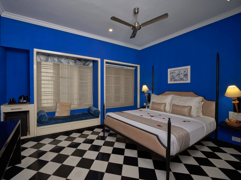 Vibrant blue hotel room at the Old Court House by Abad, with a four-poster bed and checkered floor, perfect for a stay near Fort Kochi beach.