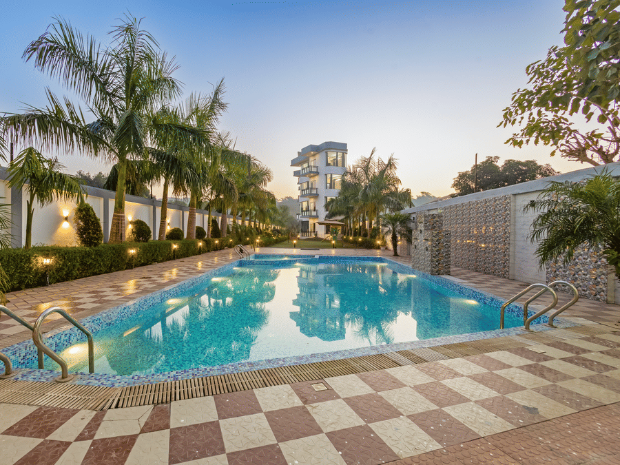 An outdoor swimming pool surrounded by palm trees and a tiled deck during the blue hour at twilight - Nature Trails Rishikesh