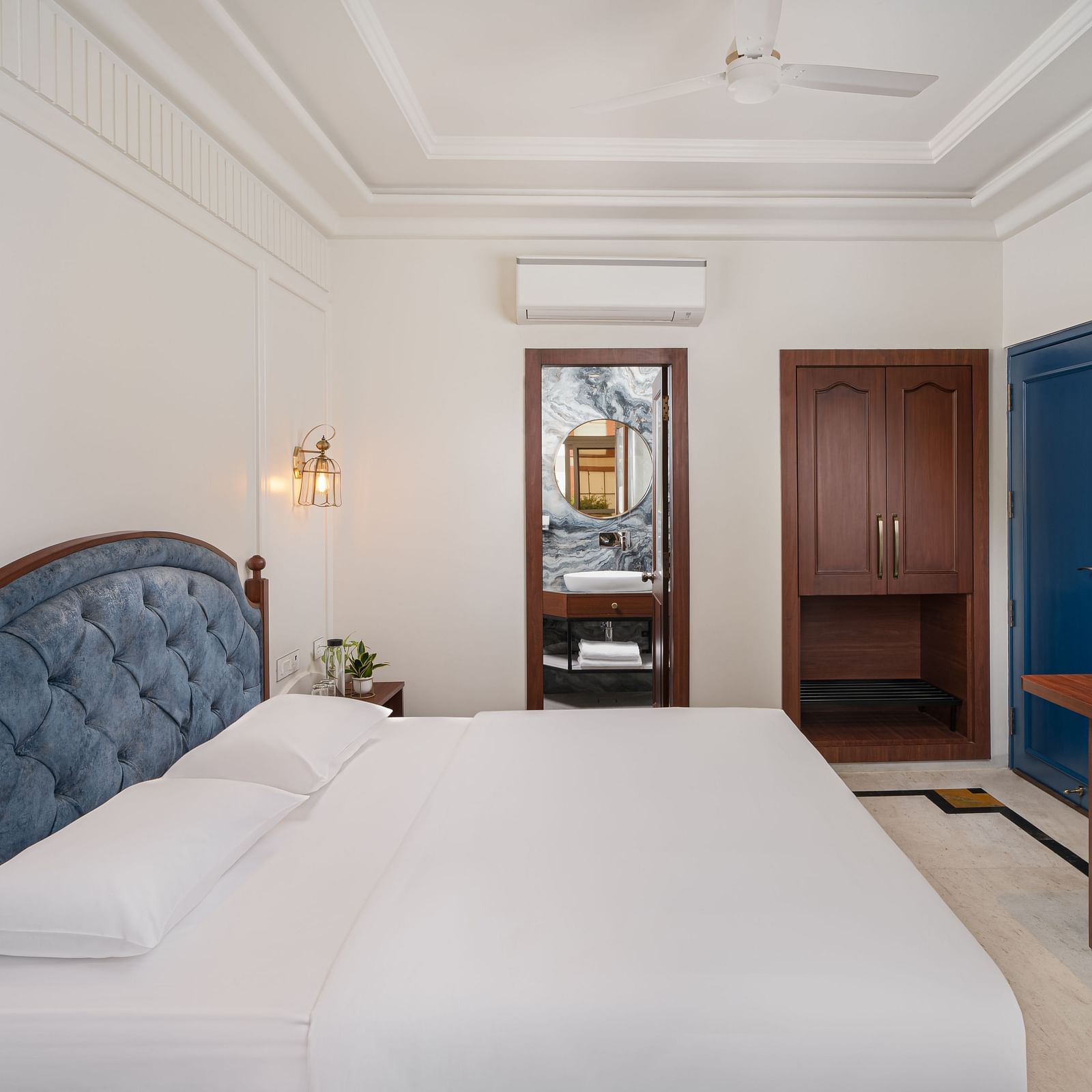 A side view of the room features a spacious bed, a wall-mounted television directly opposite the bed, and wooden furniture | Hotel Ganga Maiya