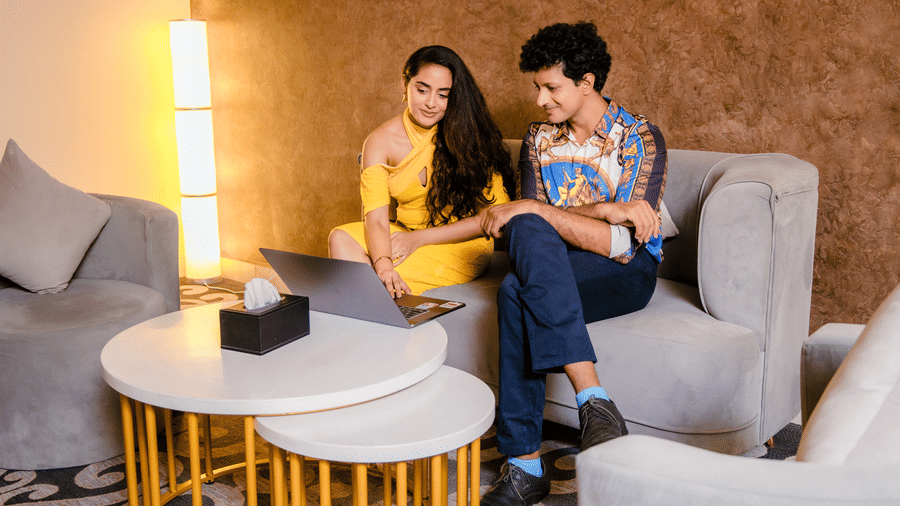 Couple using a laptop on the grey sofa in the Executive Suite living area, beside round nesting tables and a floor lamp at Ilara Hotels & Spa, Tada.
