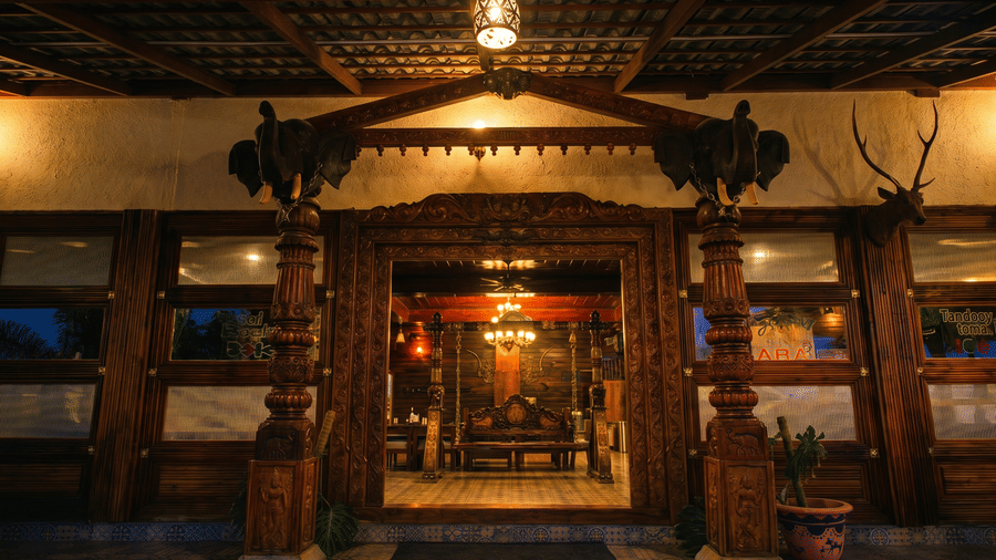 An outdoor night view of a building entrance with traditional wooden pillars and doors | Vintage Trails By Ilara