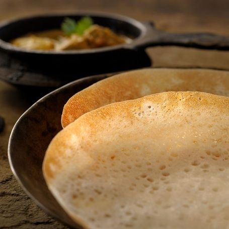 Fluffy appam and curry in a traditional pot.