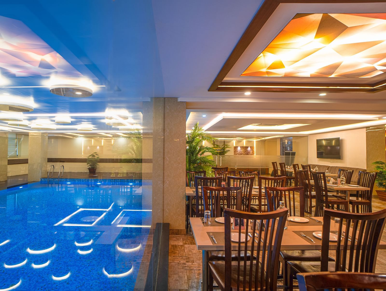Poolside dining area with chairs, tables, and ceiling lights beside the indoor pool at Mansha Regency, Port Blair.