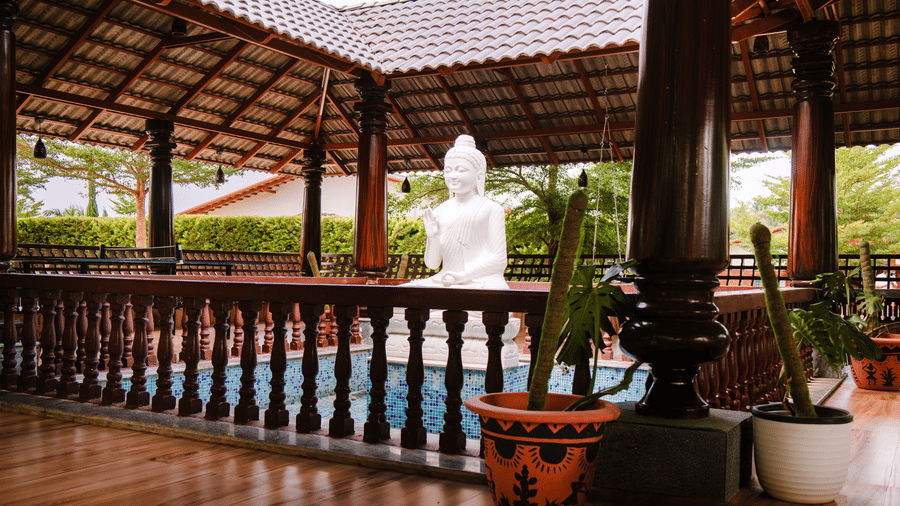 A covered outdoor balcony with wooden railings and pillars overlooking a white Buddha statue | Vintage Trails By Ilara