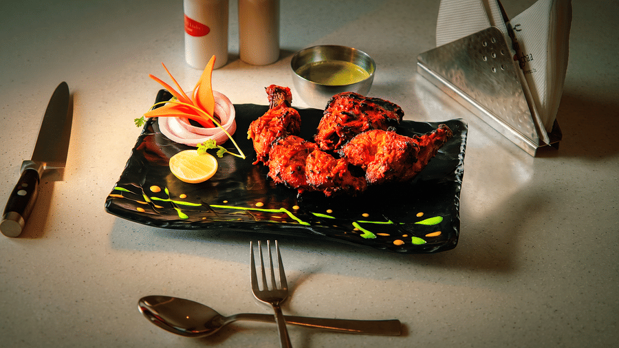 Tandoori chicken pieces on a black platter with onion rings, lemon, a carved carrot flower and green chutney at Tandoori Tamashaa, Ilara Hotels & Spa, Tada.