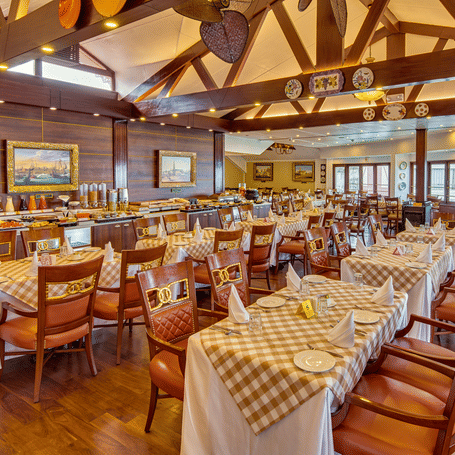 A large, airy banquet hall or function room, with many tables set for a meal, featuring white and gold tablecloths, red chairs, and exposed wooden ceiling beams.