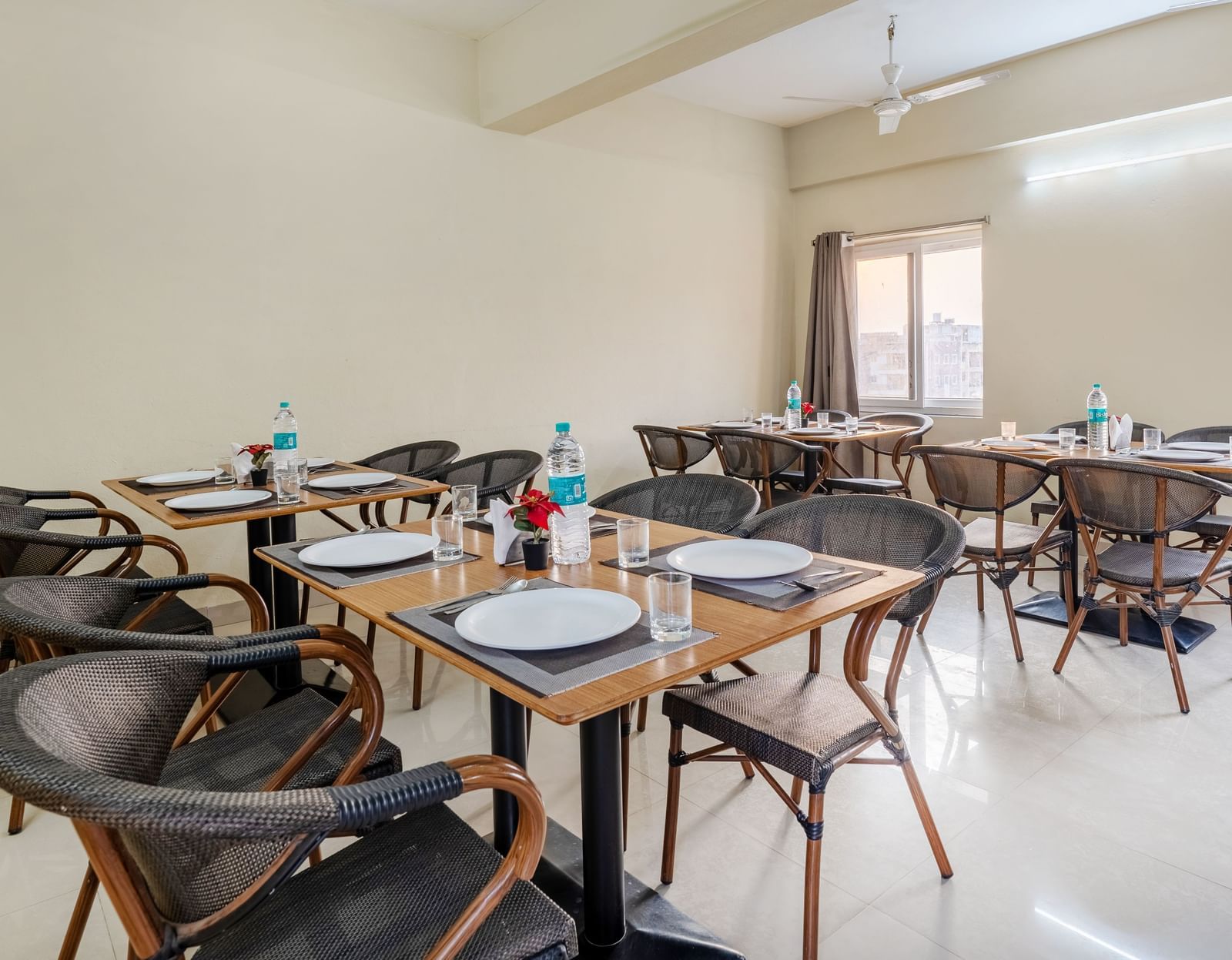 A dining area at Destino by Monday Hotels, Gachibowli, with 2 dining tables and woven chairs, set up with plates and water bottles.