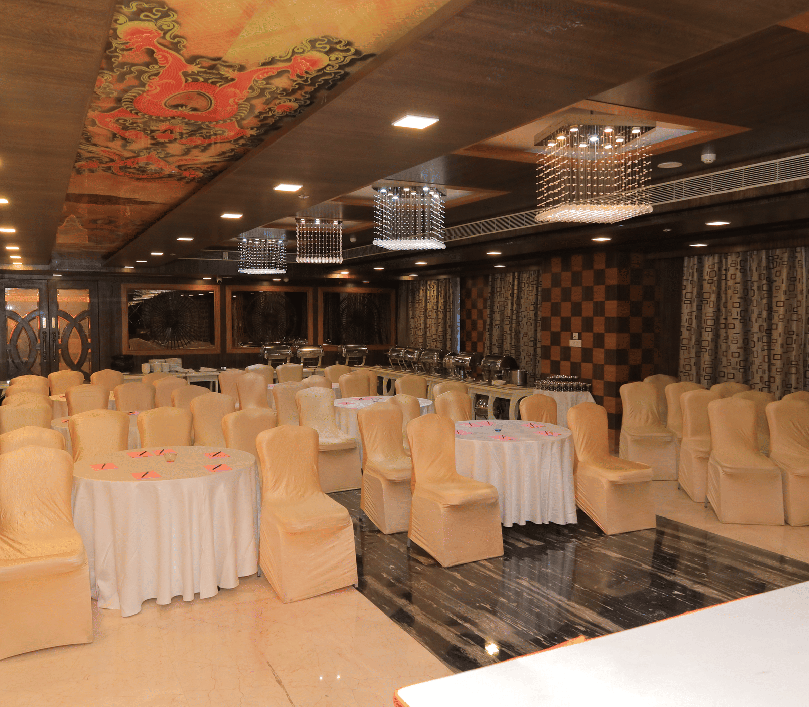 Corner view of the Bentley hall at Benzz Park, Vellore, featuring chairs surrounding round tables facing towards the stage in front of them.