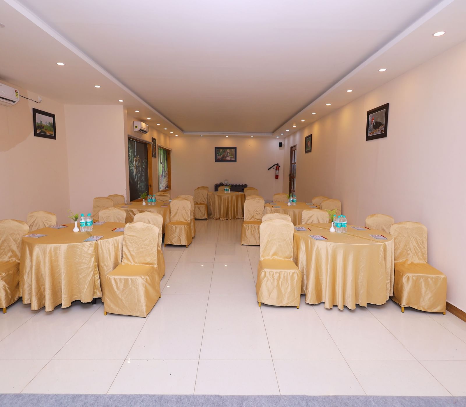 An empty banquet hall set up with tables and chairs draped in white and yellow linen at Corbett Nirvana Resort.