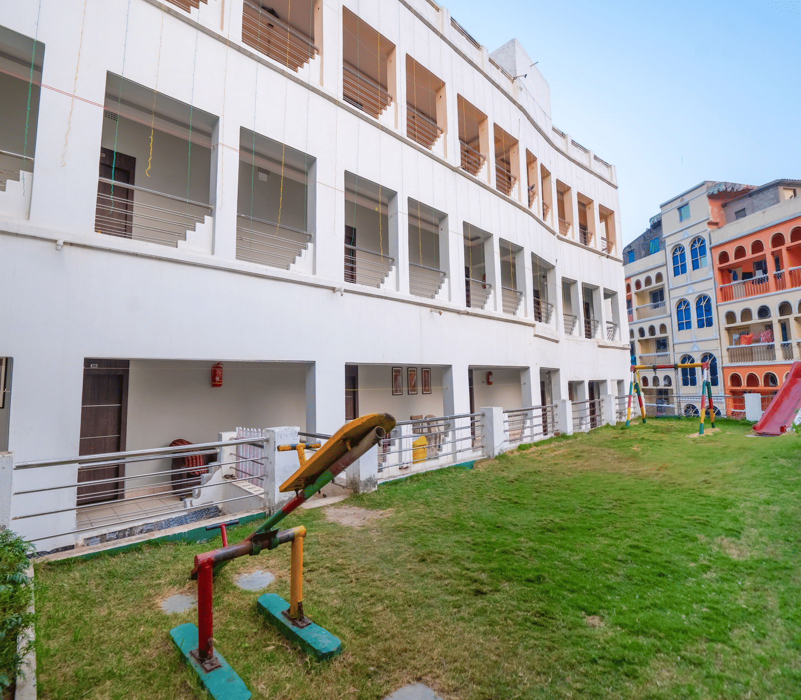 The exterior of a multi-storey, white modern hotel building surrounding a central courtyard with a green lawn and a small children's play area - Hotel Dolphin Puri