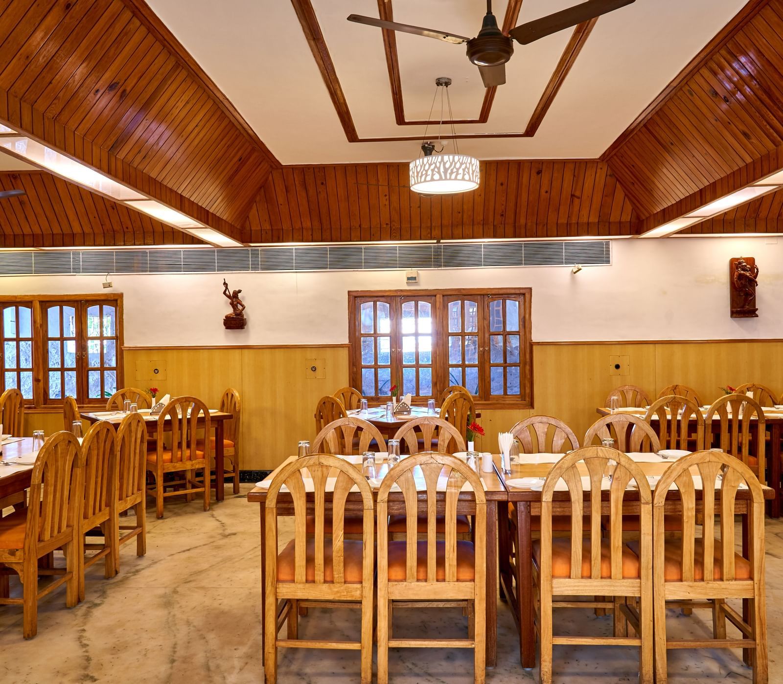 A spacious restaurant dining area at Hotel Mamallaa Heritage, filled with numerous wooden tables and chairs under a high ceiling.