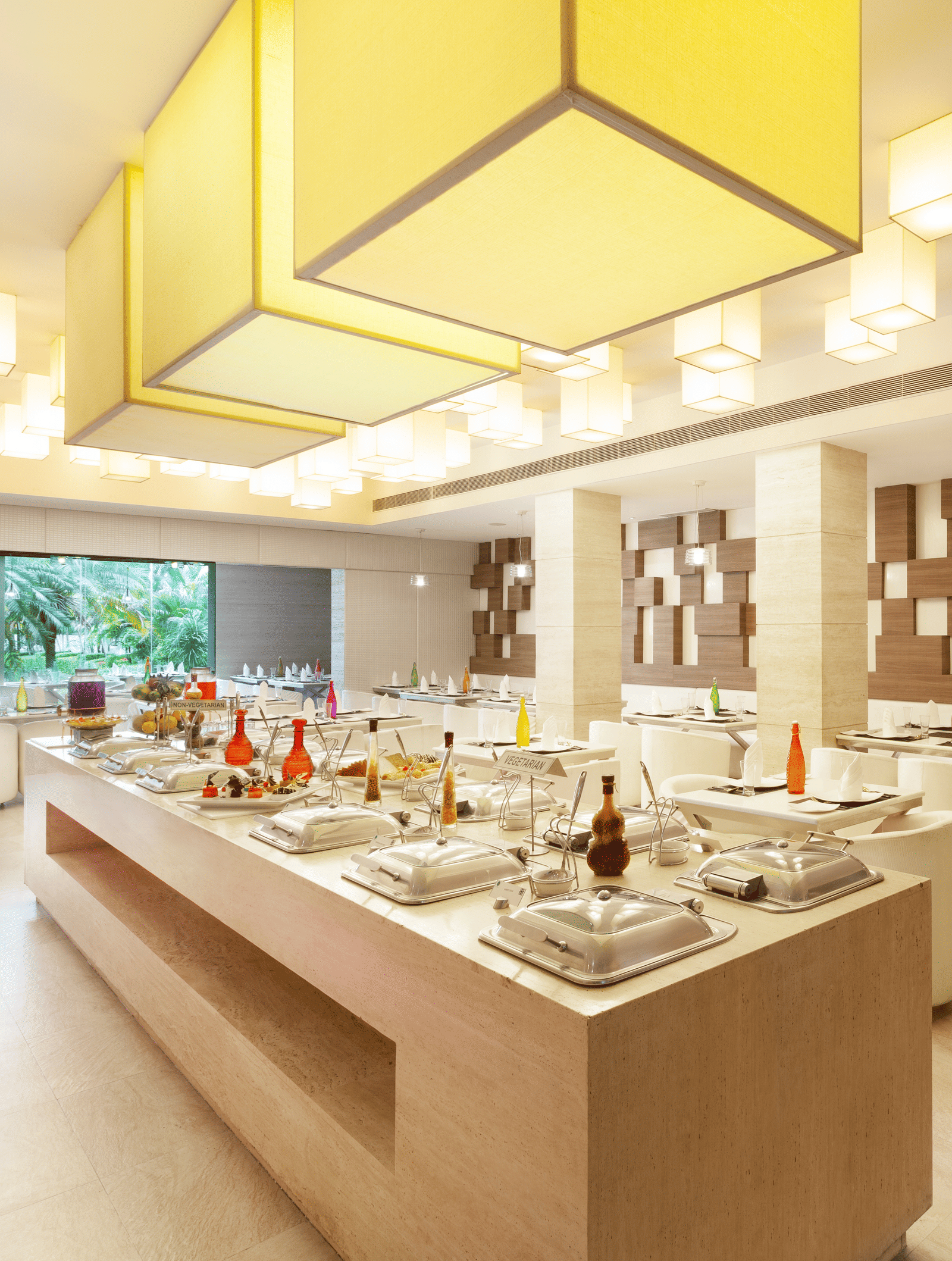 A diagonal view of a restaurant with an island in the middle featuring buffet items, surrounded by tables and chairs on the sides | Cenneys Gateway