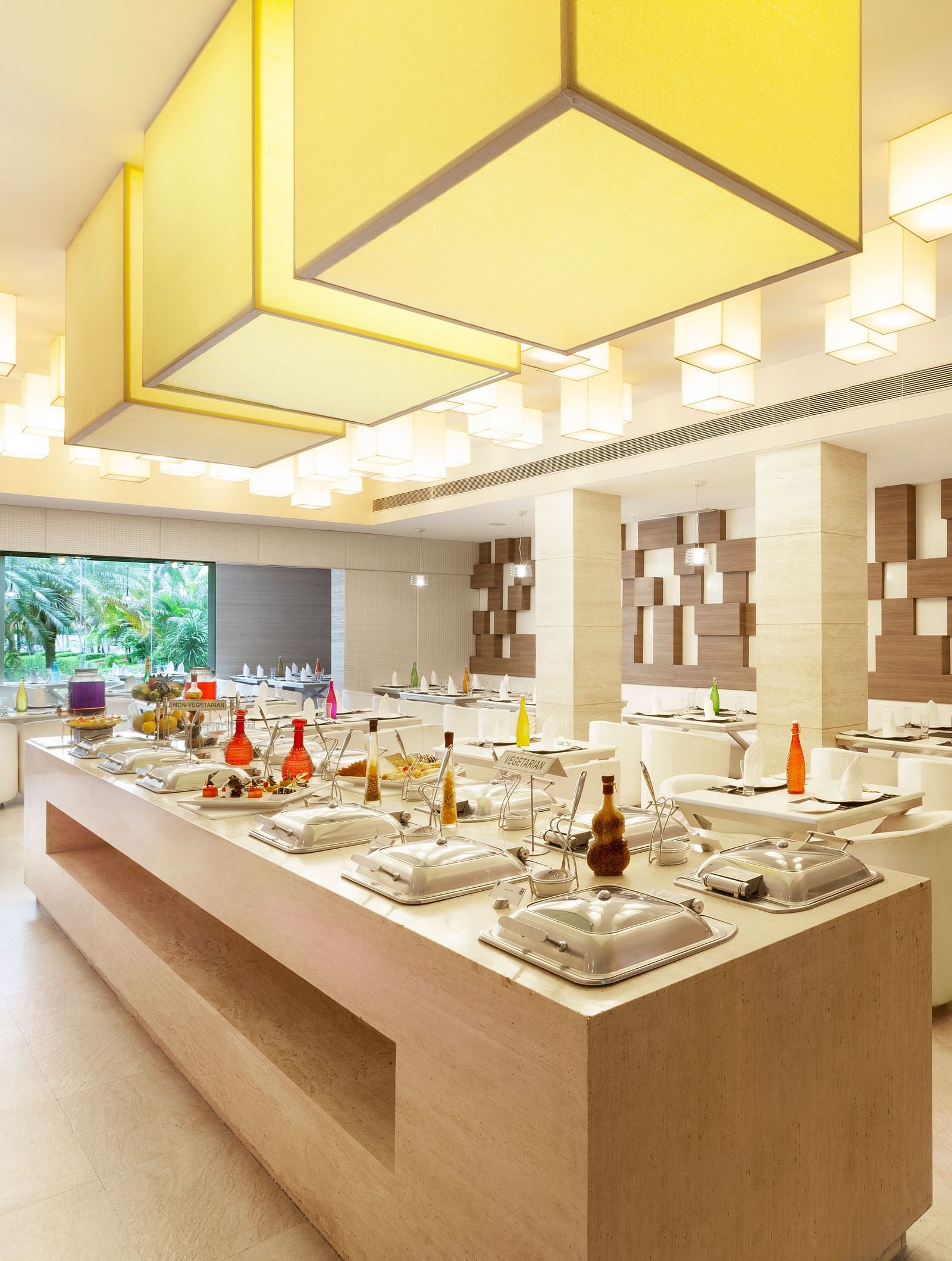 A diagonal view of a restaurant with an island in the middle featuring buffet items, surrounded by tables and chairs on the sides | Cenneys Gateway