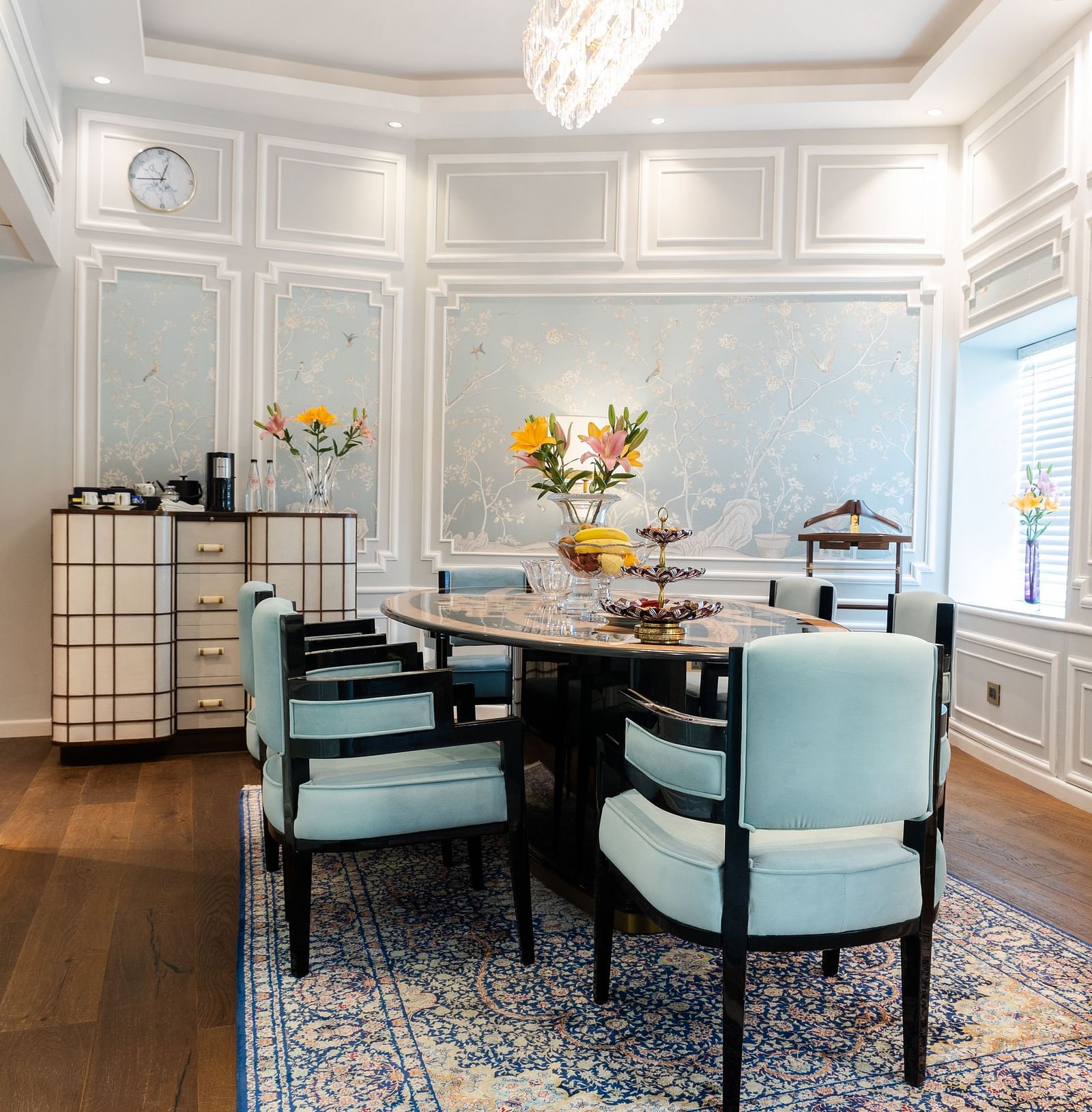 A dining table with blue cushioned chairs on either side in the living area of our Diplomatic suite in New Delhi at the Claridges