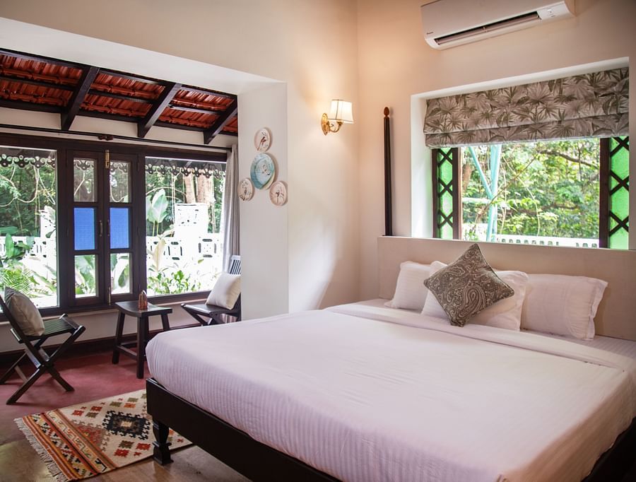 An image of a bed with big windows on the side with greenery outside at Lamrin Ucassaim Hotel, Goa
